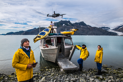 Man with crew members from scientific expedition send a drone near the vessel docked on iceberg rock bay at wintertime to explore the island